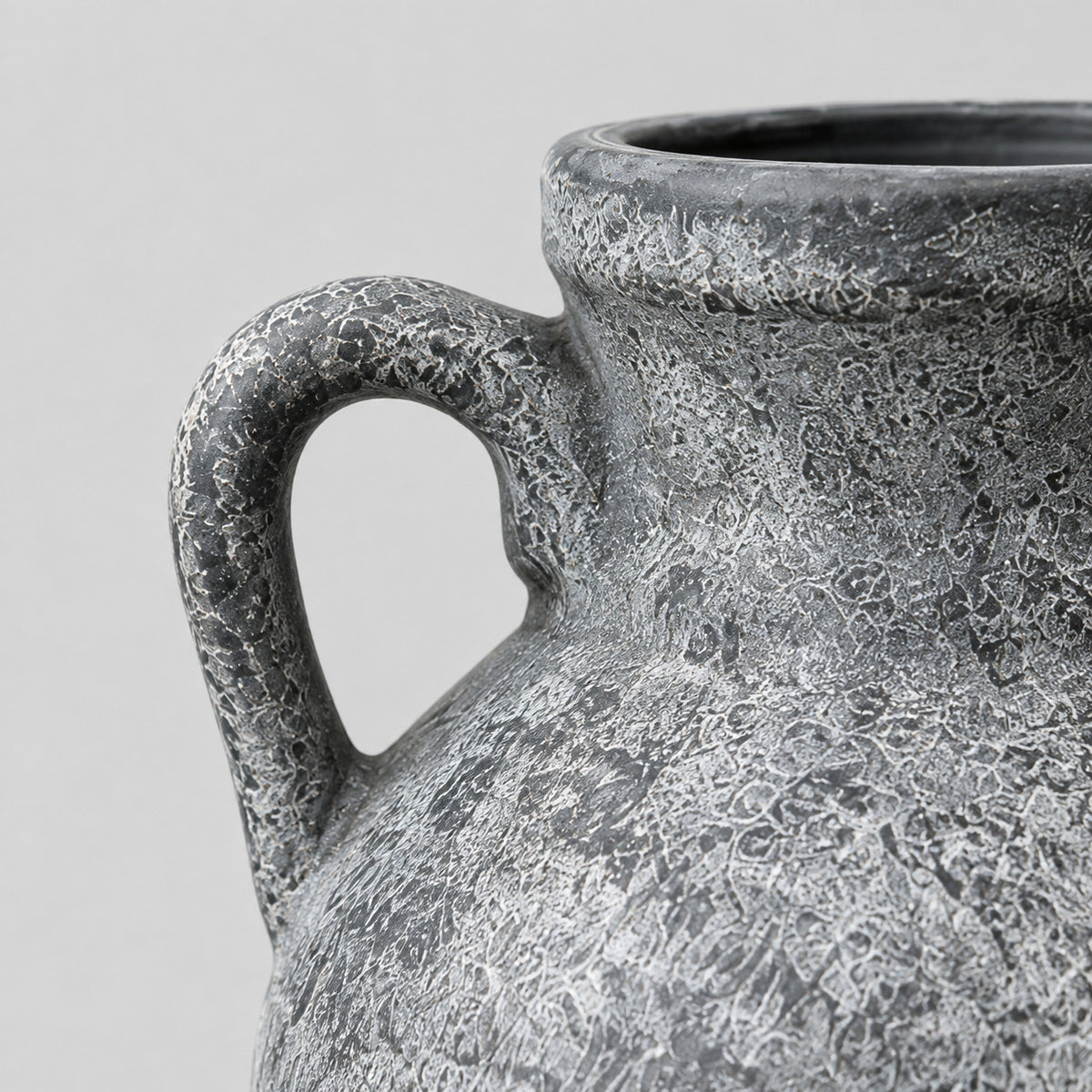 Close up of the curved side handle of the weathered gray ceramic amphora vase