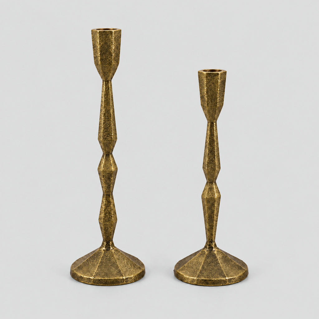 Set of two faceted cast iron taper candle holders in Antique Brass on a light gray studio background