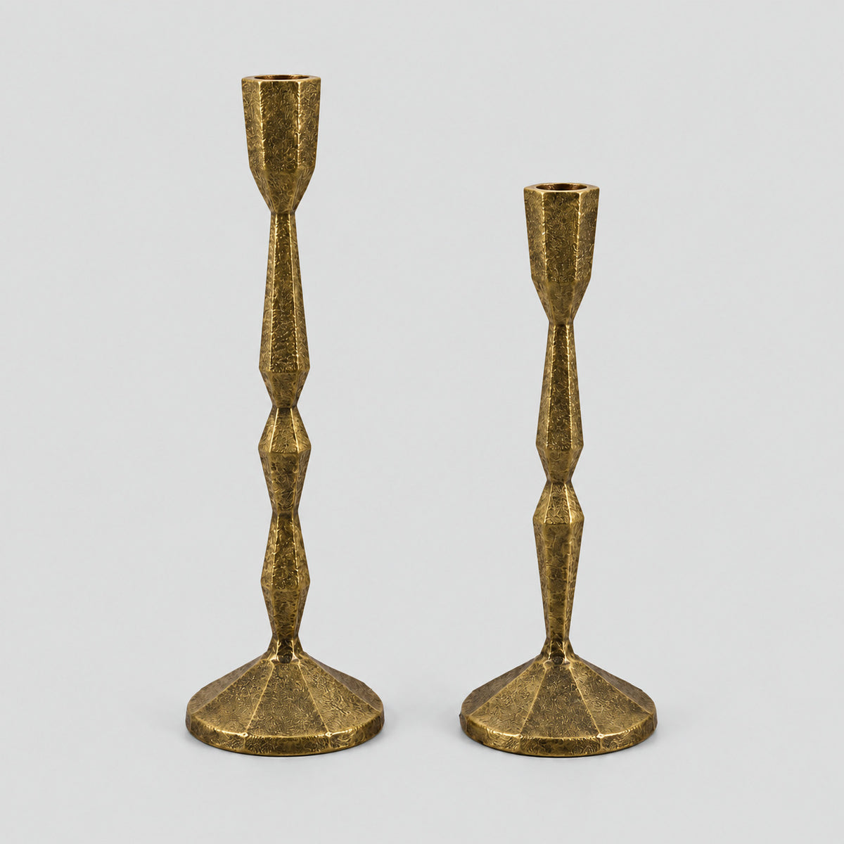 Set of two faceted cast iron taper candle holders in Antique Brass on a light gray studio background