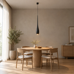 Matte Black slender teardrop pendant light lit hanging above a 90 cm round oak dining table in a daylight room.