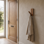 Natural Acacia fold-down wooden coat hook mounted on the plaster wall of an entryway beside a 90 cm wide front door with one linen coat on the hook