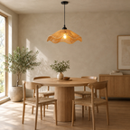 Wavy woven rattan pendant light lit hanging above a 90 cm round oak dining table against a plain wall