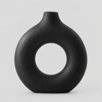 Hollow round ceramic vase in matte black on a light neutral gray studio background.