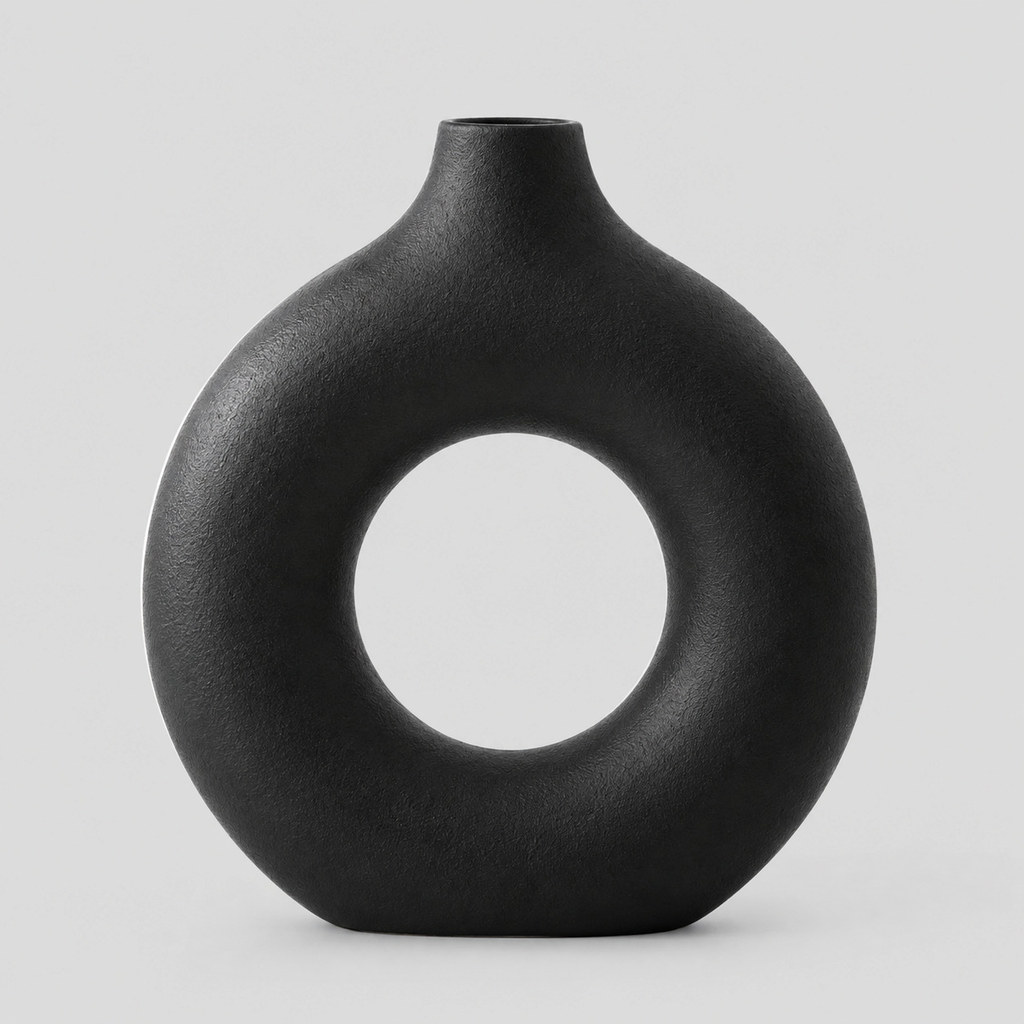Hollow round ceramic vase in matte black on a light neutral gray studio background.