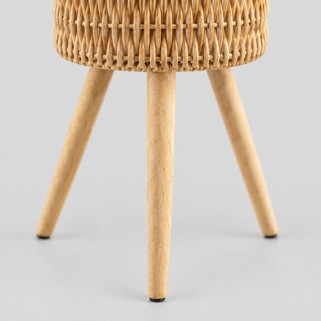 Close up of the tapered wooden foot of the standing woven rattan planter basket on wooden tripod legs in Natural Rattan.