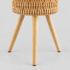 Close up of the tapered wooden foot of the standing woven rattan planter basket on wooden tripod legs in Natural Rattan.