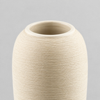 Close up of the smooth rounded rim at the mouth of the off-white tall ribbed stoneware vase.
