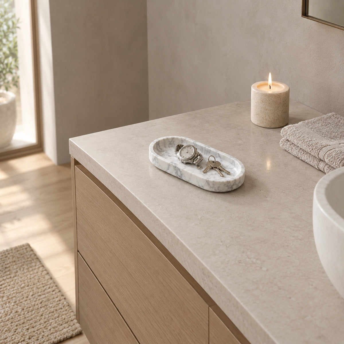 Oval carved stone catchall tray in Carrara White on a bathroom vanity with keys and a watch.