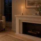 Brushed brass taper candle holder on a mantelpiece with one lit taper candle in the holder.