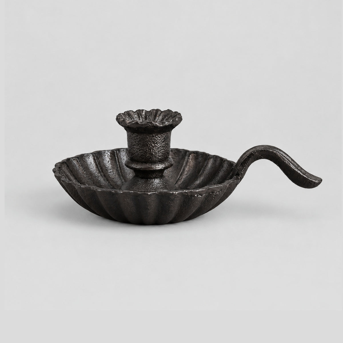 Cast iron chamberstick candle holder in Cast Iron on a light gray studio background.